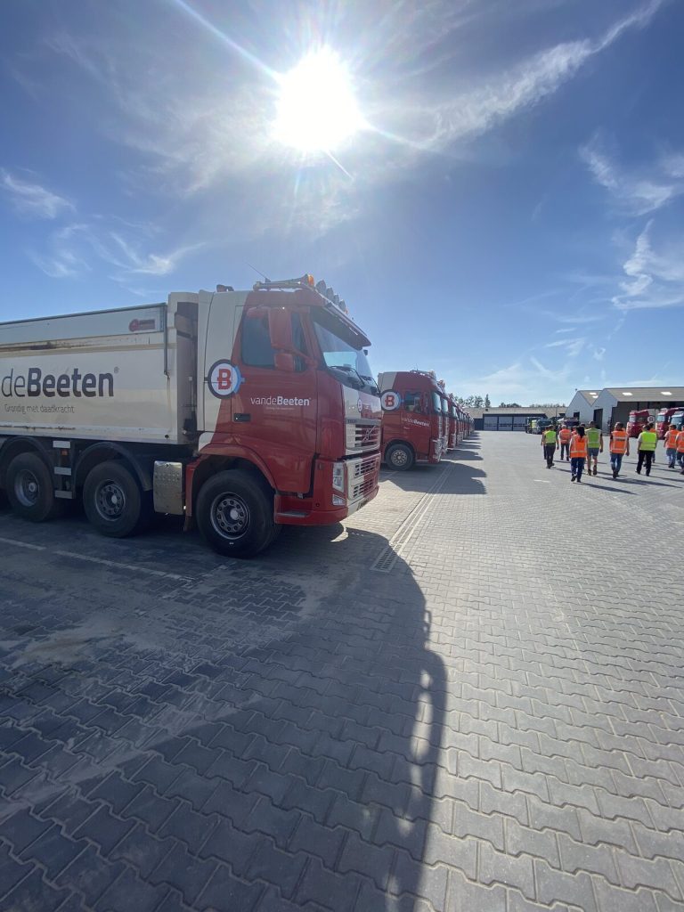 Deelnemers in veiligheidshesjes lopen langs het wagenpark van Van de Beeten tijdens het locatiebezoek